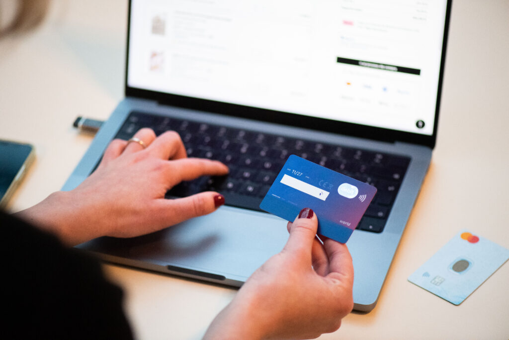 A person paying online with a bank card held next to a laptop
