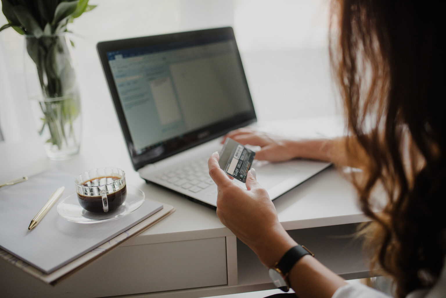 Close-up of a person looking at a credit card while working at a laptop.