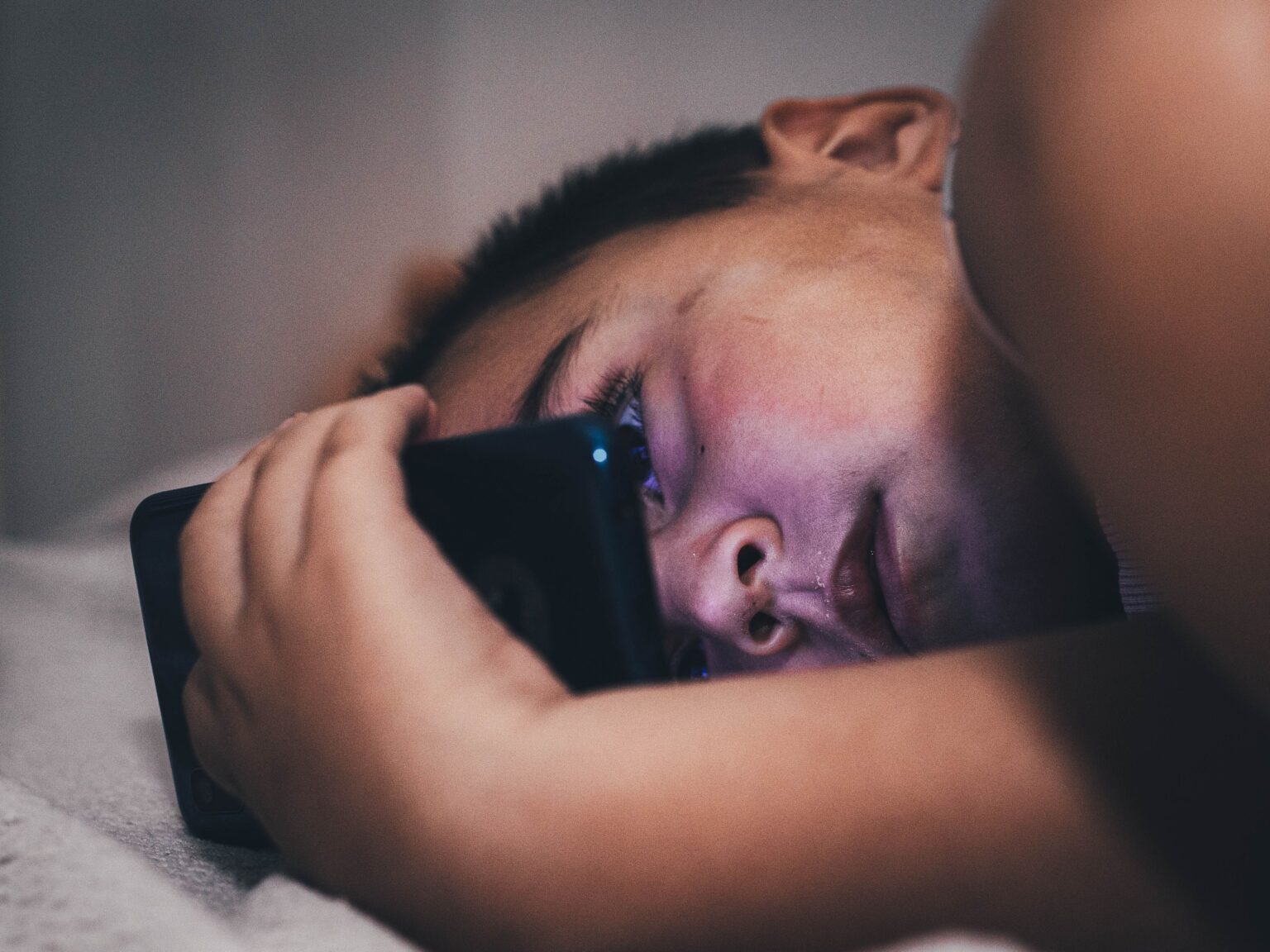A teenager using a smartphone at night, lit only by the screen